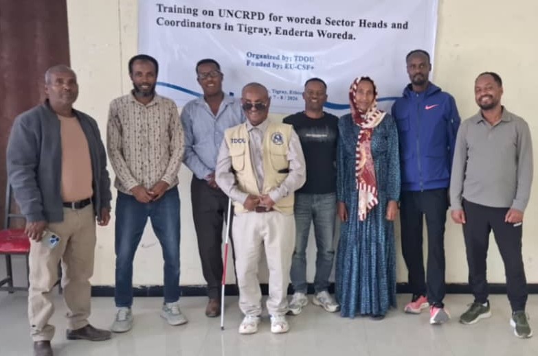 Eight participants pose for a group photo during a UNCRPD training organized by TDOU in Enderta Woreda, standing in front of an event banner.