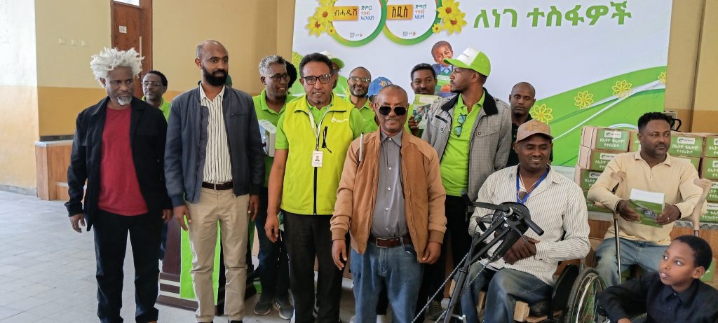 A group of about fifteen men posing together in front of an Ethio telecom banner, some in green Ethio telecom shirts and vests, others using a wheelchair, a white cane and crutches, several holding exercise books, with a young boy in front.